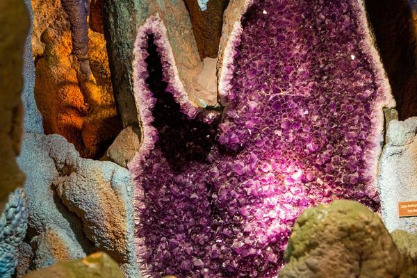 A large amethyst geode with purple crystals surrounded by rough rock formations.