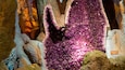 Eine große Amethyst-Geode mit violetten Kristallen, umgeben von rauen Felsformationen.
