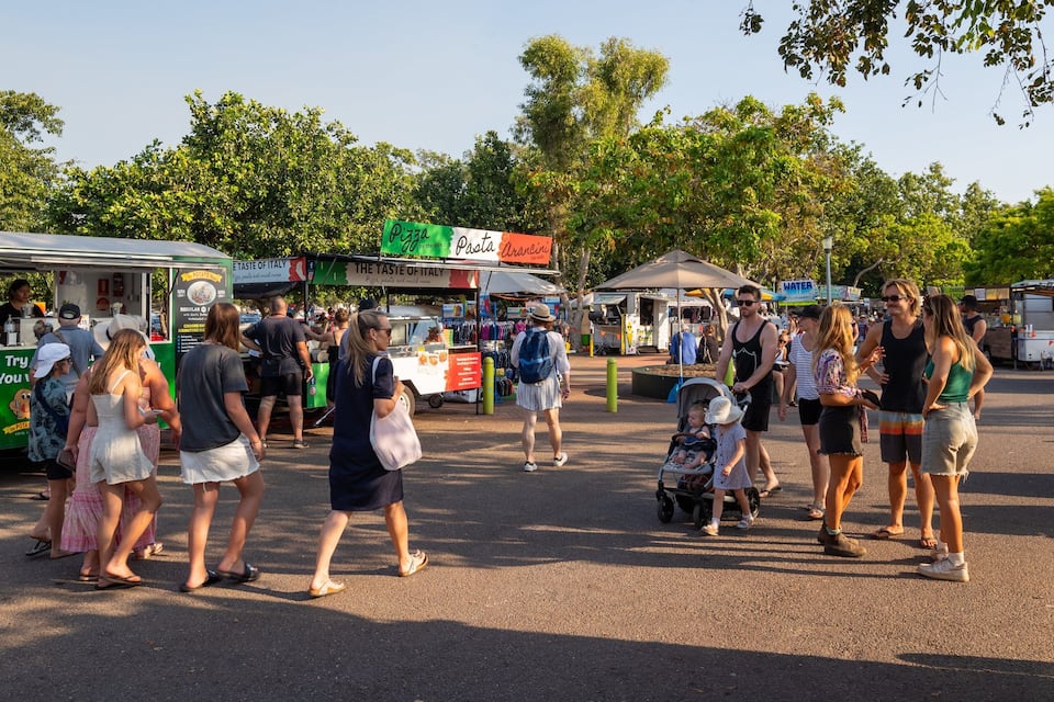 A busy outdoor market with food stalls and people walking around.