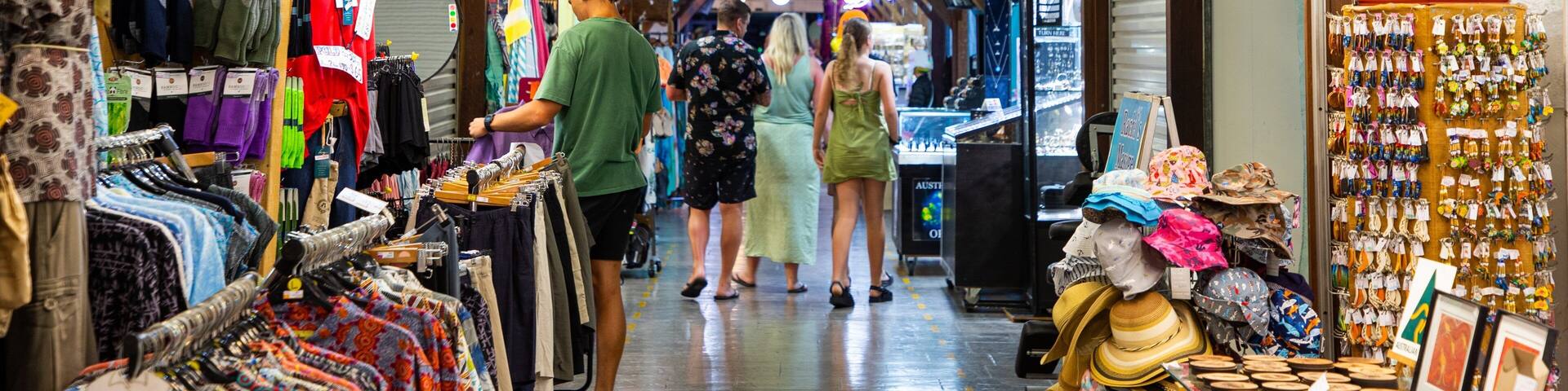 A narrow market aisle with clothing racks, hats, and accessories.
