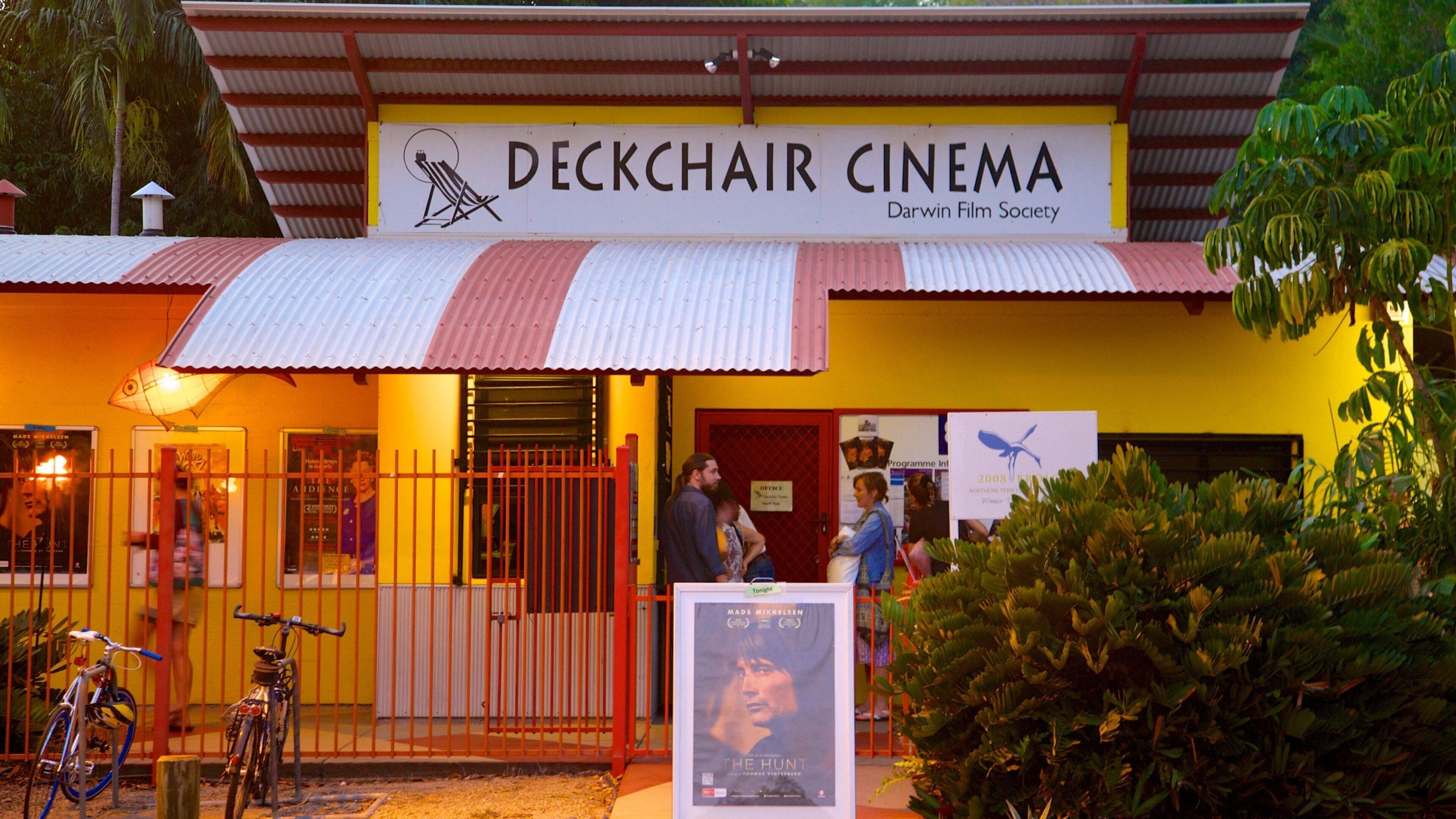 A cinema named 'Deckchair Cinema' with a signboard, a red and white roof, and a poster for 'The Hunt' movie.