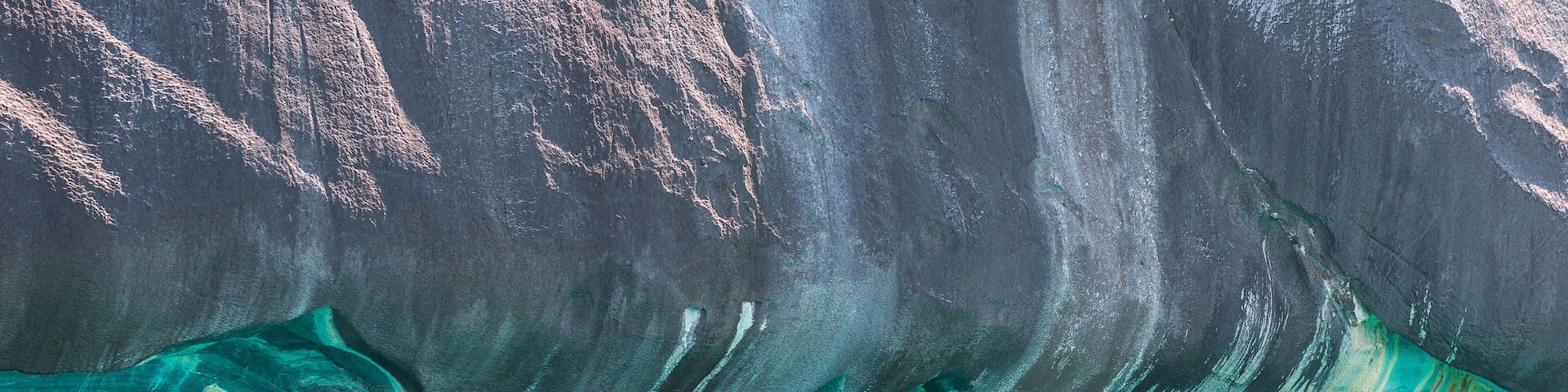 A large rock formation with a cave-like opening and turquoise water.