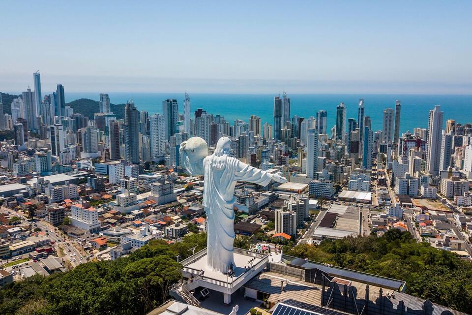 A cityscape with a prominent statue of a figure with outstretched arms, surrounded by high-rise buildings and a coastline in the background.