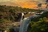Een waterval stort neer over rotsen, omgeven door weelderige begroeiing.