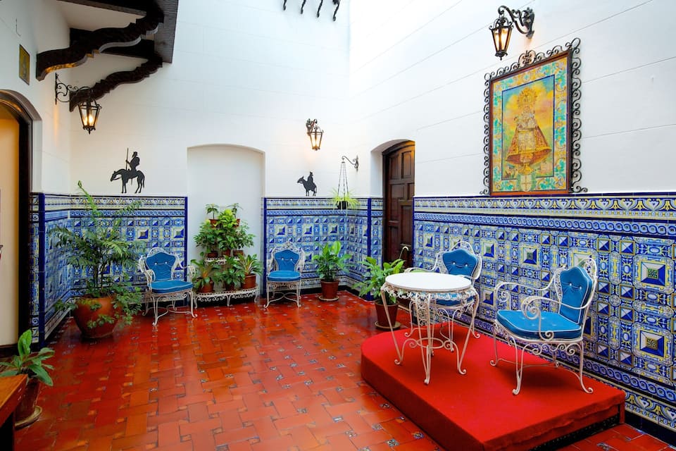 A courtyard with blue and white tiled walls, a red carpet, and blue chairs.