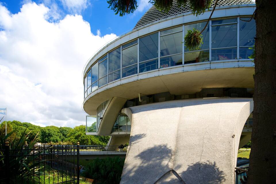 A modern building with a curved glass facade, surrounded by lush greenery and a clear blue sky.