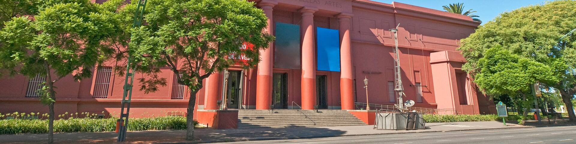 Un museo con fachada roja, amplias columnas y un cielo azul despejado.