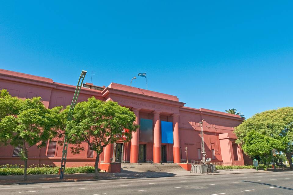A museum with a red facade, large columns, and a clear blue sky.