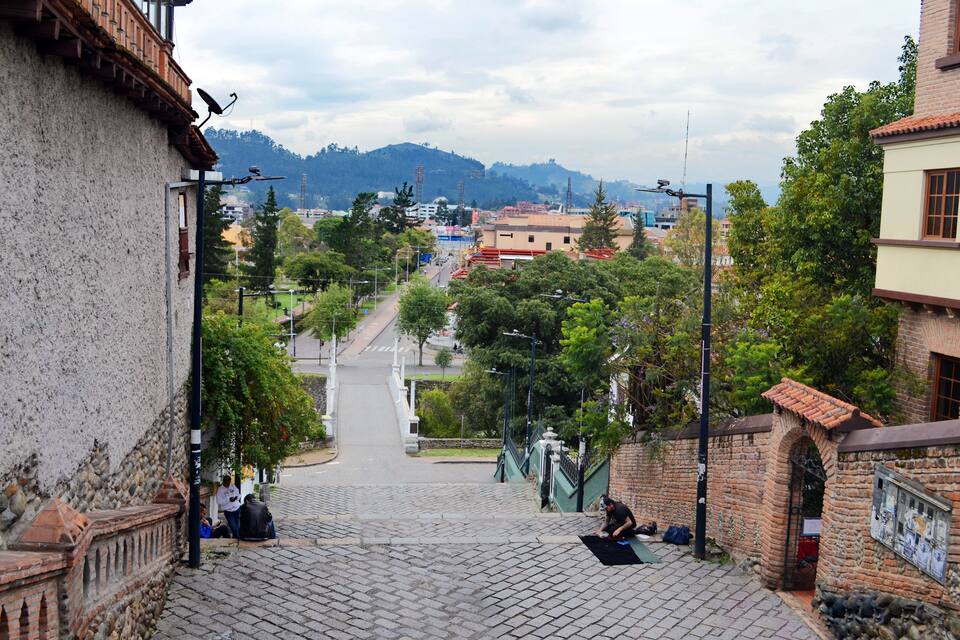 A cobblestone street leading to a town square with a view of distant hills.