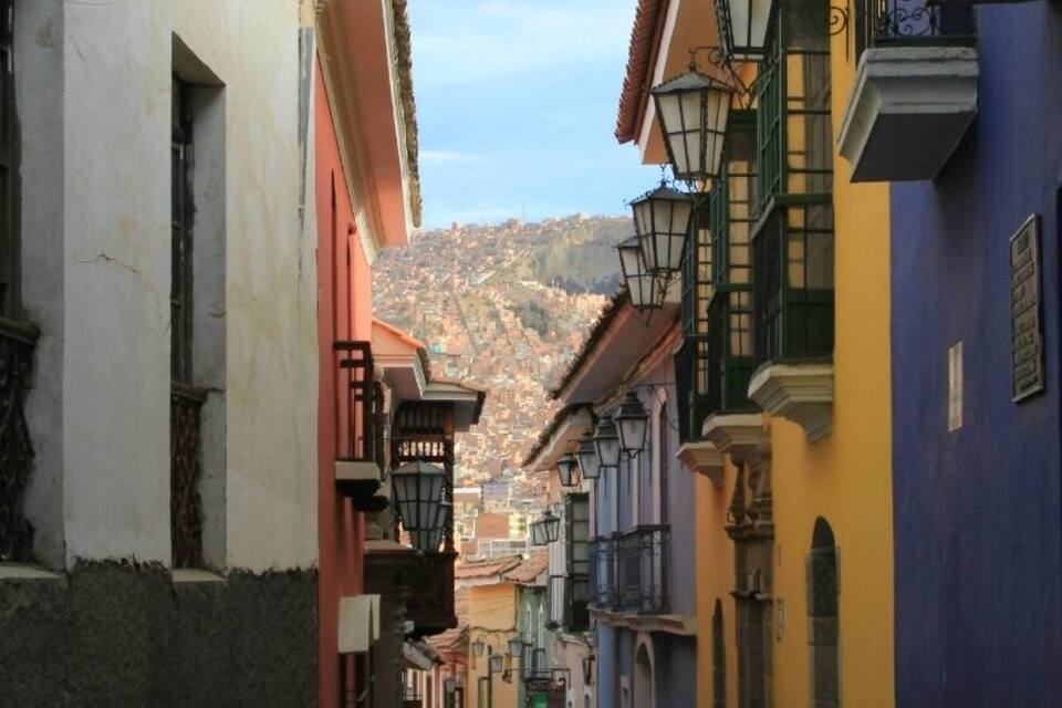 Uma rua de paralelepípedos ladeada por edifícios coloridos, com uma montanha ao fundo e algumas pessoas caminhando.