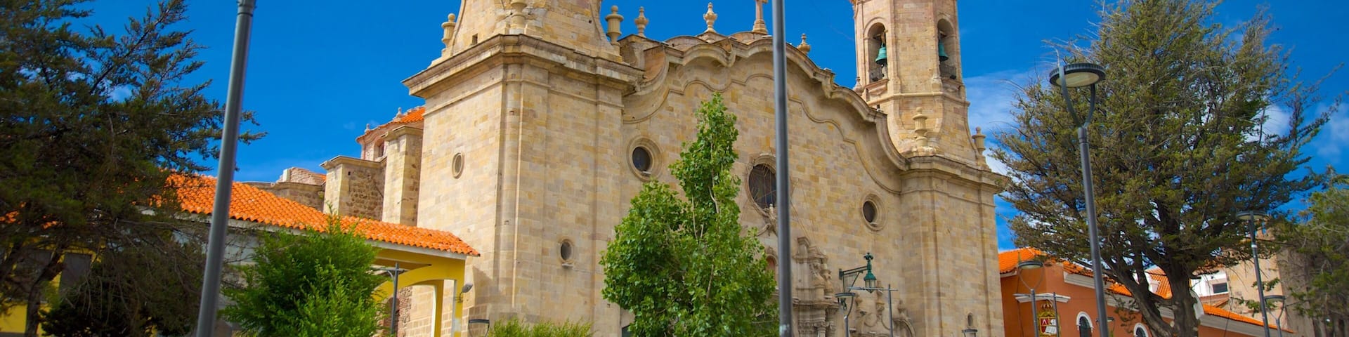Una iglesia histórica con dos torres de campanas y un reloj, rodeada de árboles y faroles.