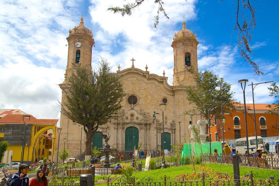 A historic church with two towers, surrounded by a vibrant public square with people and greenery.