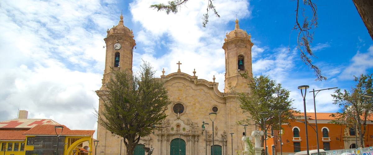 A historic church with two towers, surrounded by a vibrant public square with people and greenery.