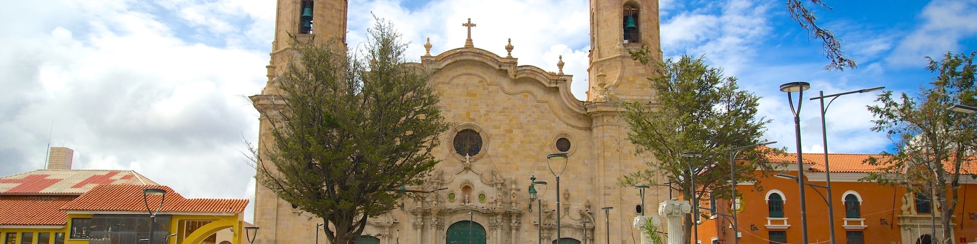 A historic church with two towers, surrounded by a vibrant public square with people and greenery.