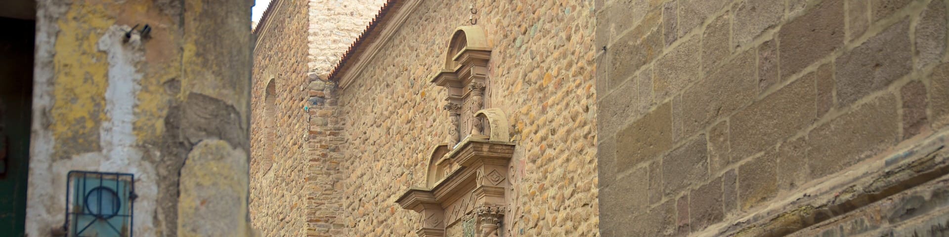Una calle estrecha con edificios de piedra, una cruz verde y una señal de límite de velocidad.