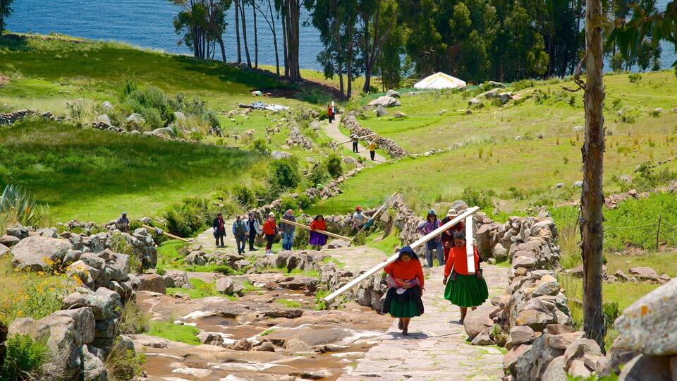 A group of people walking on a stone path surrounded by rocks and greenery, with a lake and trees in the background.