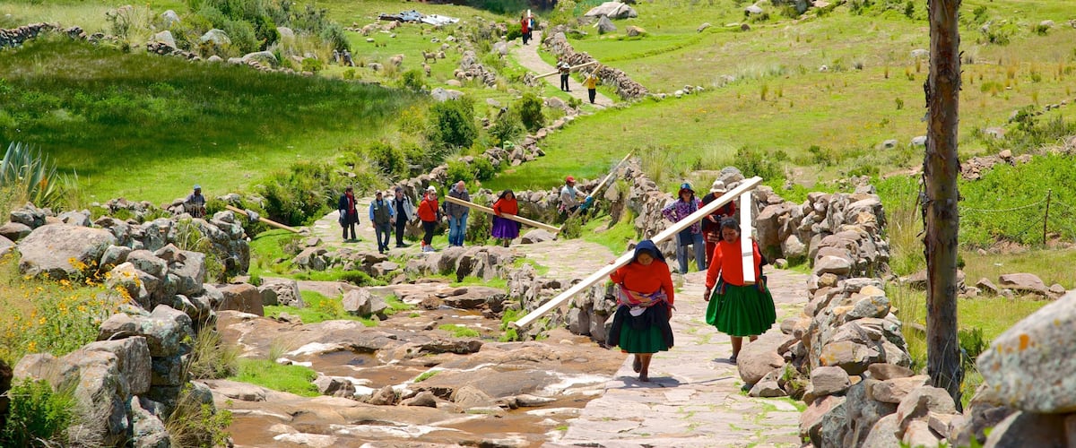 A group of people walking on a stone path surrounded by rocks and greenery, with a lake and trees in the background.