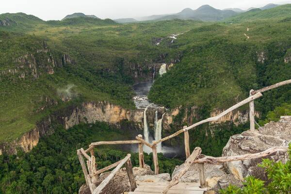Un escalier en bois mène à un point de vue d’où l’on peut admirer une cascade et une rivière, le tout étant entouré de collines verdoyantes.