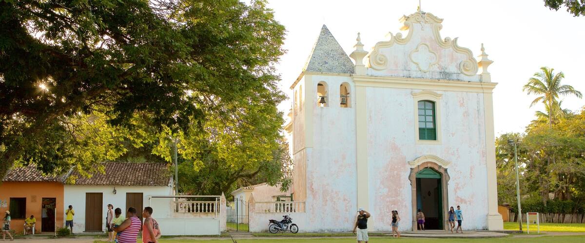 A colonial-style church with a white facade and green window, surrounded by a grassy area and palm trees.