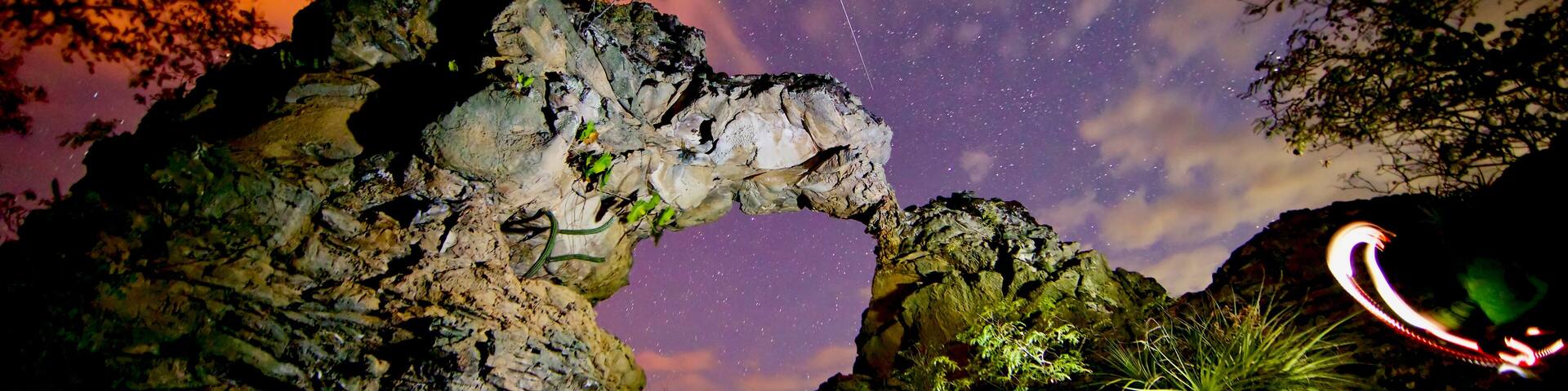 Una formación rocosa con un arco natural y un cielo nocturno estrellado.