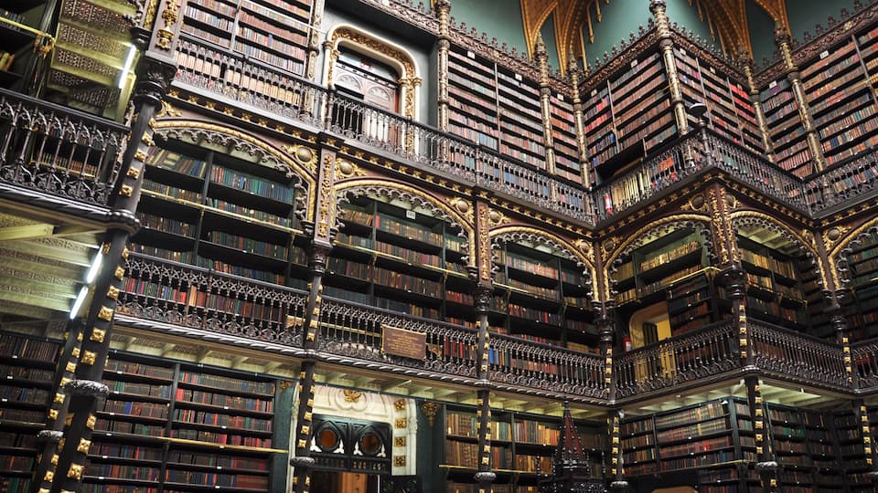 Une bibliothèque somptueuse et richement décorée, avec de nombreuses étagères réparties sur plusieurs niveaux et des détails architecturaux complexes.