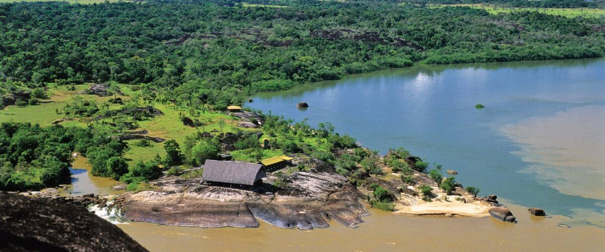 A river winding through a lush landscape with a small house on a rocky outcrop.