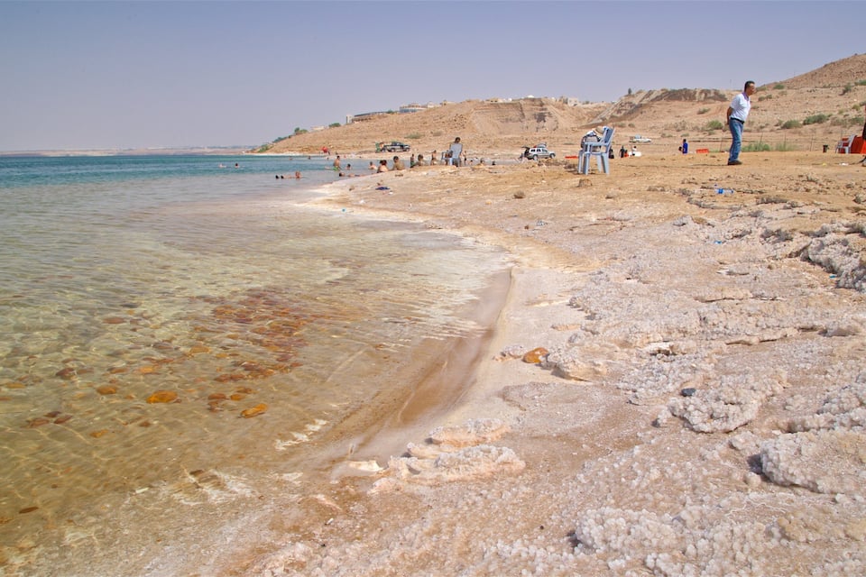 Une plage avec une eau claire et peu profonde, un rivage rocheux et des gens qui prennent des bains de soleil.