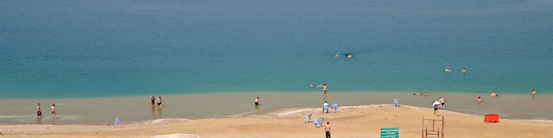 Uma praia com águas turquesa cristalinas, pessoas nadando e tomando sol, e vários guarda-sóis oferecendo sombra.