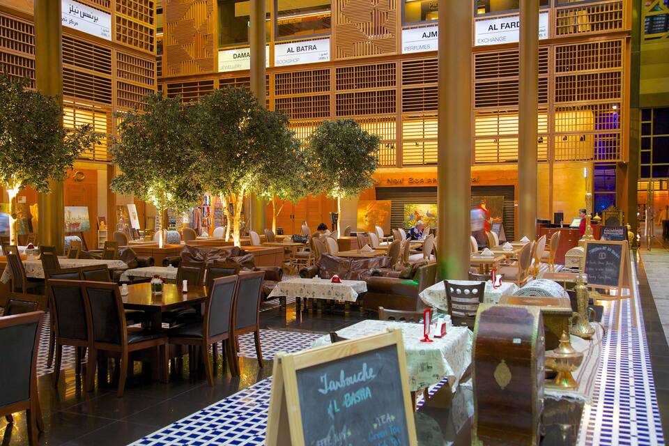 An indoor dining area with tables and chairs, trees, and illuminated signs.