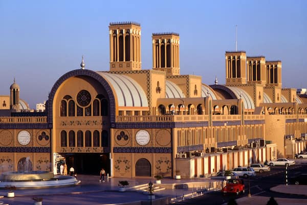 Un grand bâtiment imposant, richement décoré, doté de plusieurs dômes et de minarets, entouré d’une place avec une fontaine et des voitures.