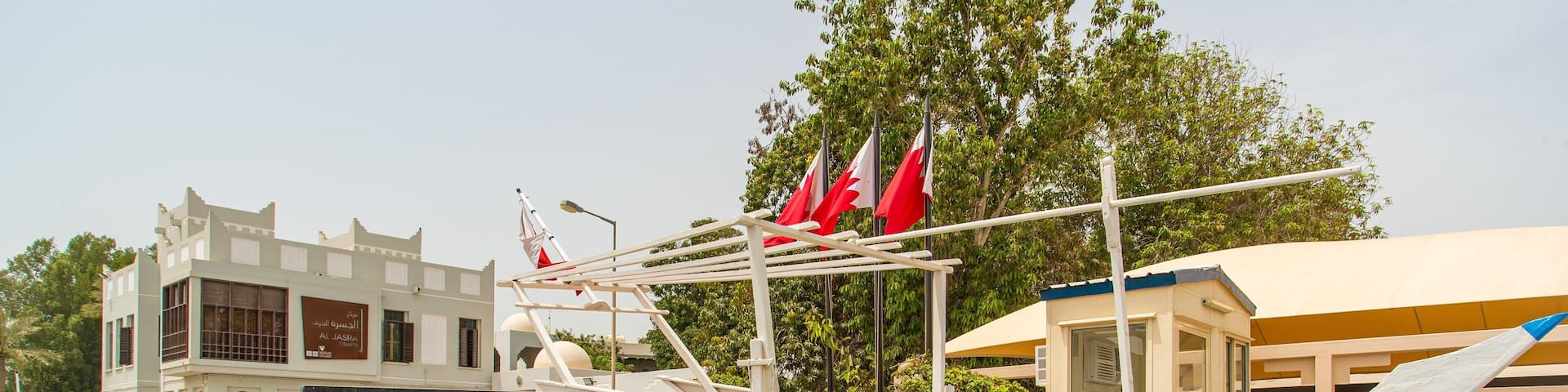 A traditional wooden boat with red flags, parked in front of the Al Jasra Handicrafts Centre.