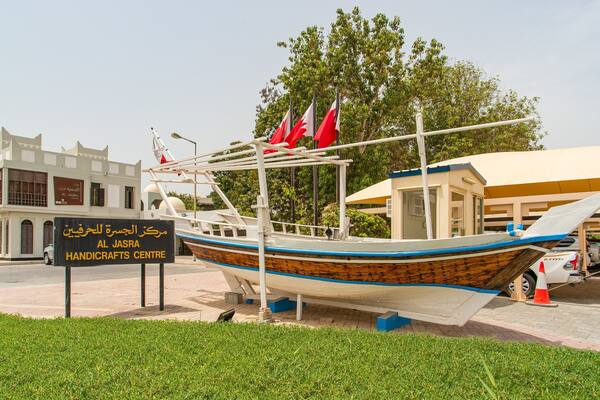 Un bateau en bois traditionnel, orné de drapeaux rouges, est amarré devant le centre d’artisanat d’Al Jasra.