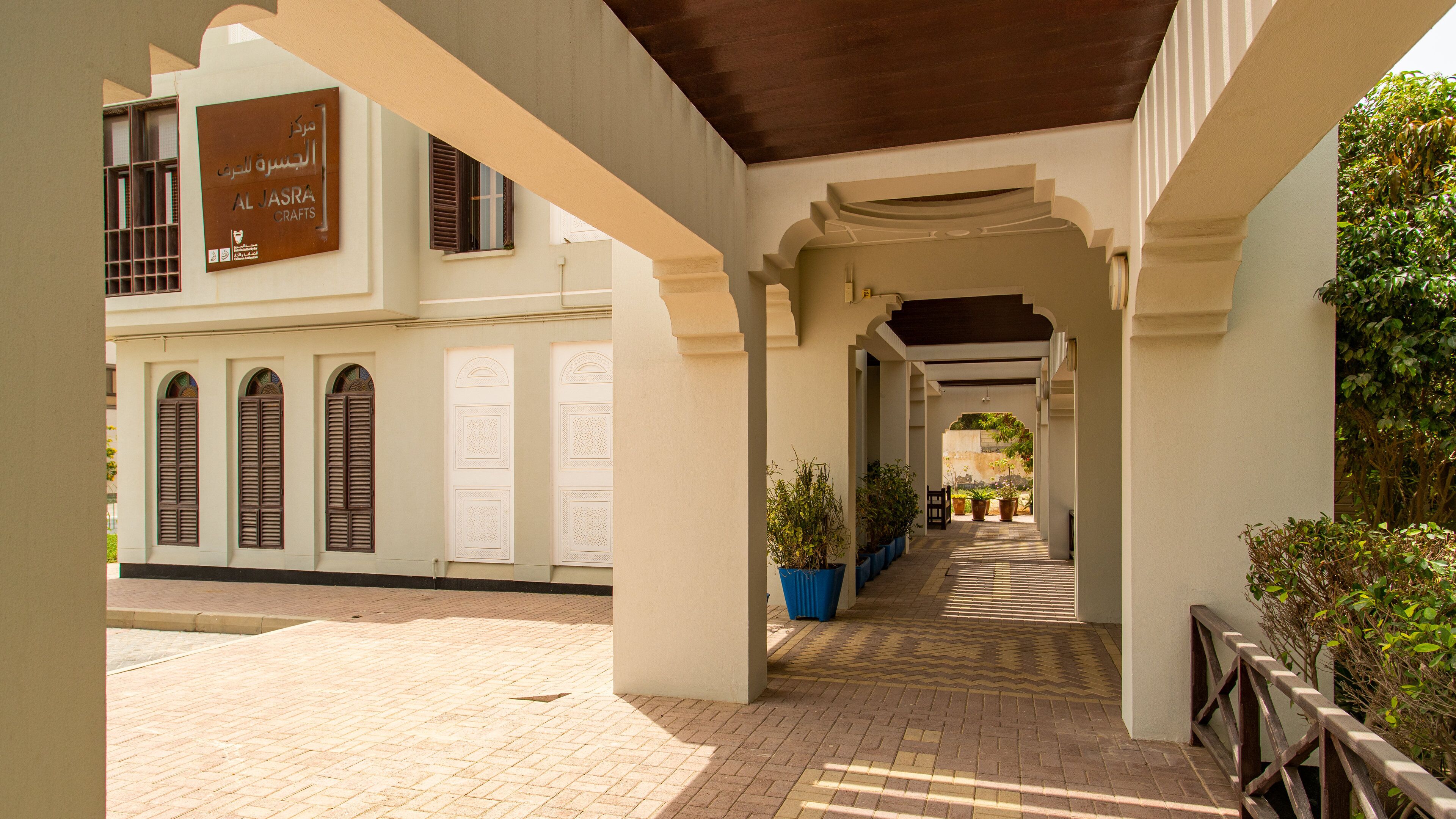 A covered walkway with arches, potted plants, and a sign for Al Jazeera Crafts.