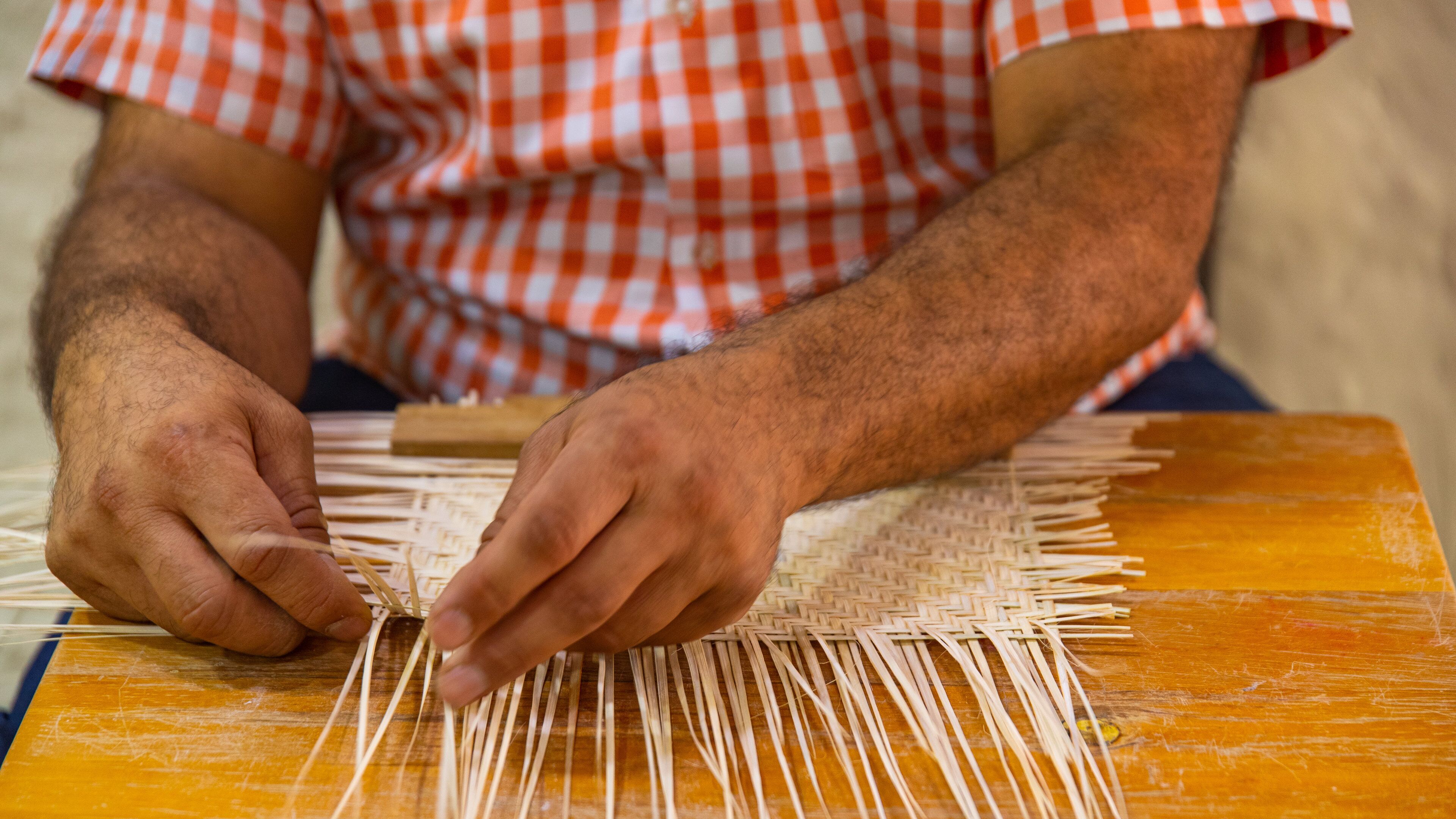 A person weaving with straw on a wooden table.