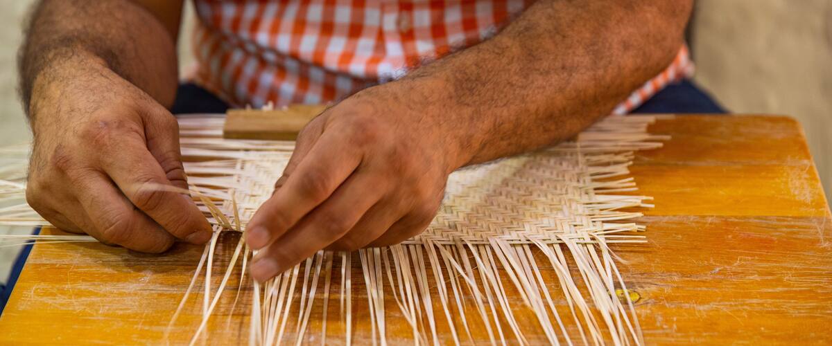 A person weaving with straw on a wooden table.