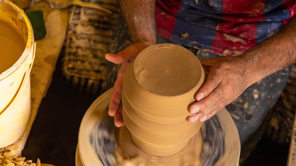 A person shaping a clay pot on a pottery wheel.