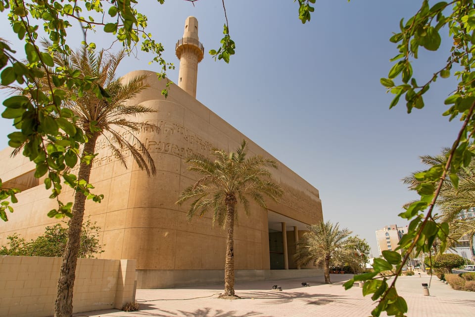 A mosque with a tall minaret and palm trees in the foreground.
