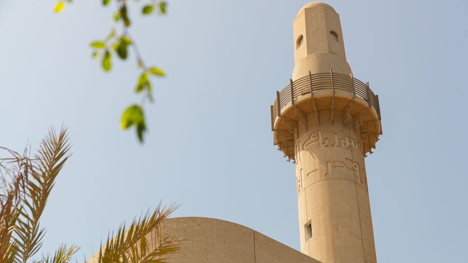 A tall minaret with Arabic calligraphy, surrounded by palm trees.