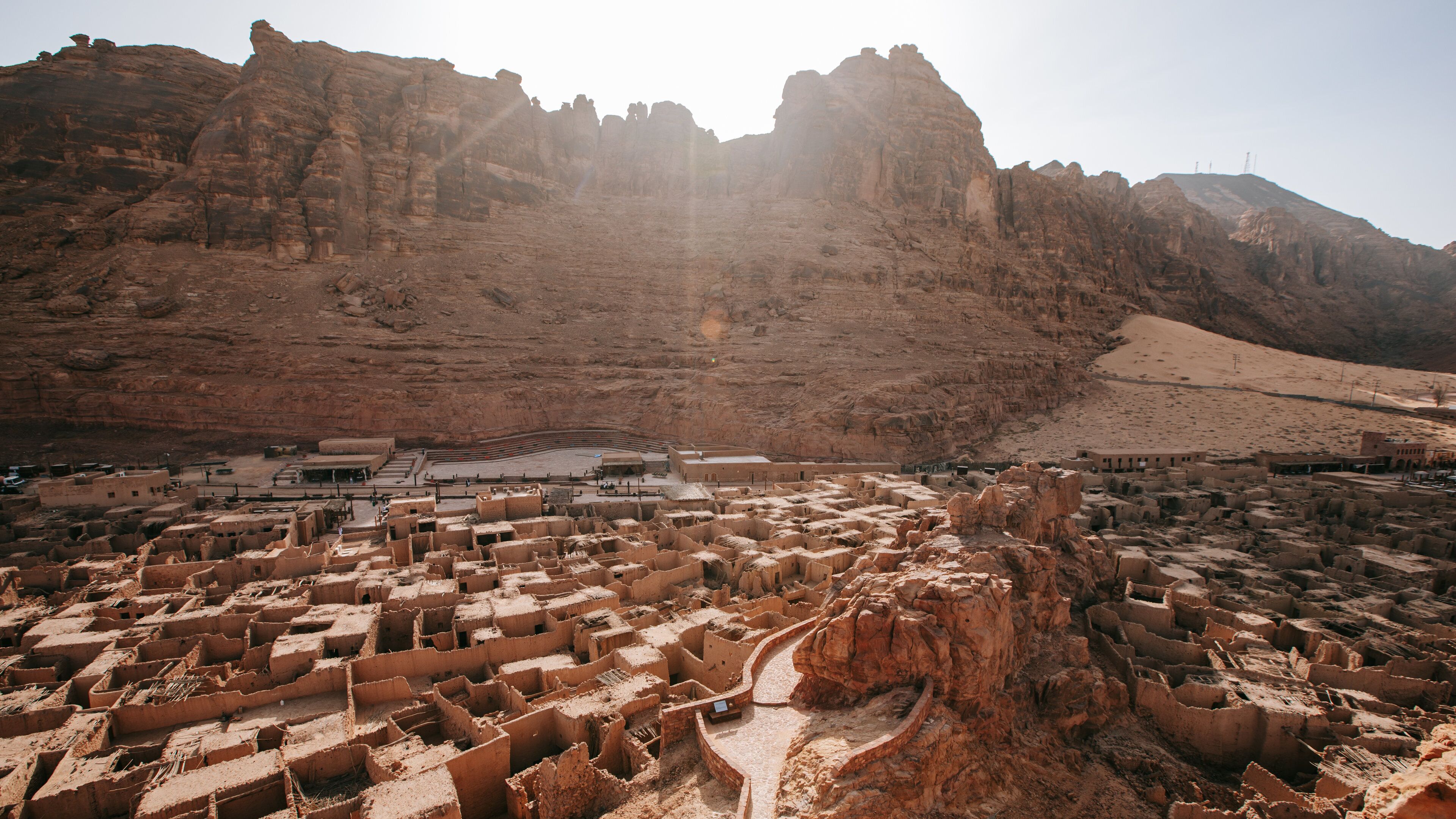A desert landscape with ancient mud-brick ruins and a large rock formation.