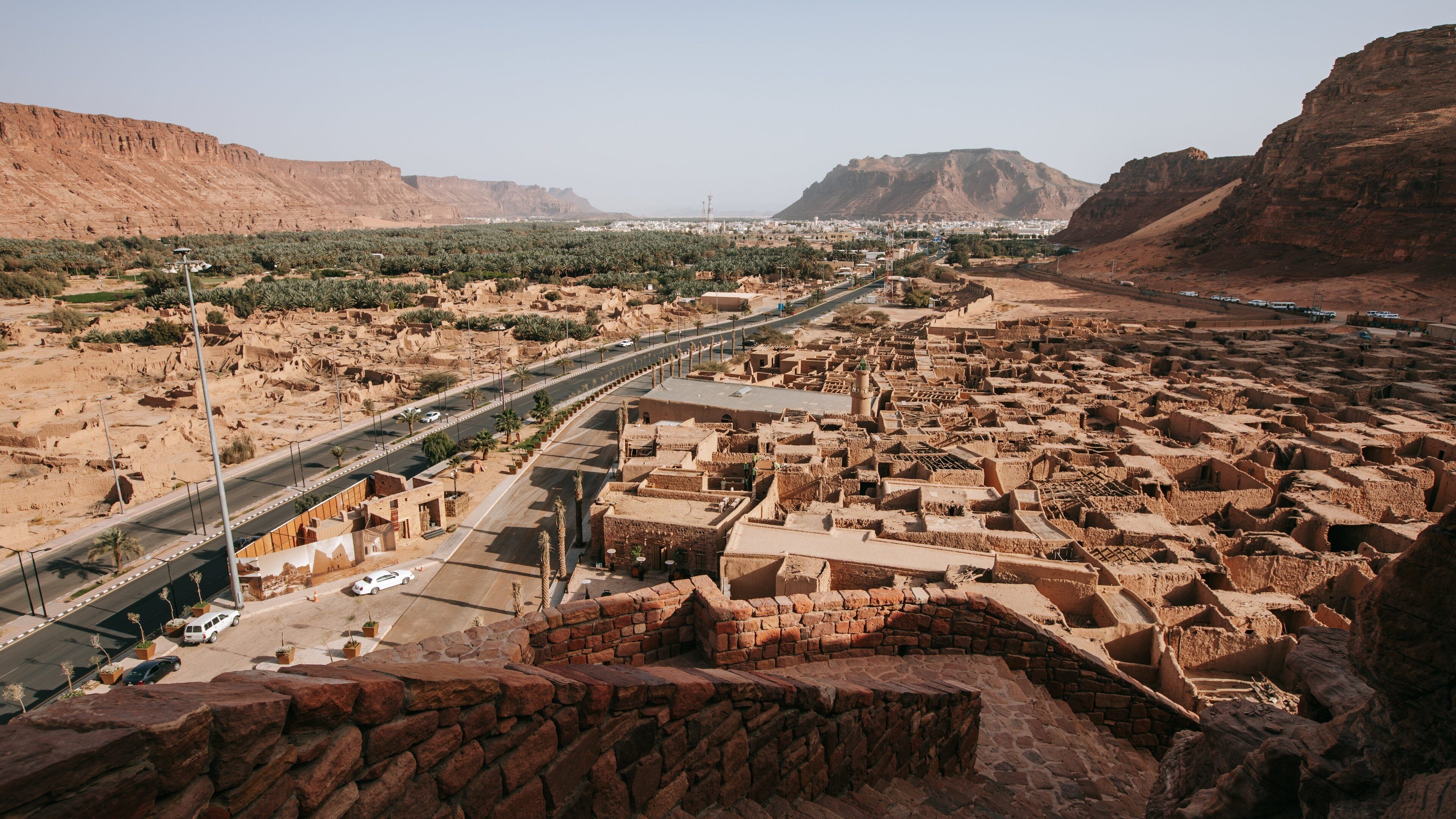 A desert landscape with a modern highway, traditional mud-brick buildings, and distant mountains.