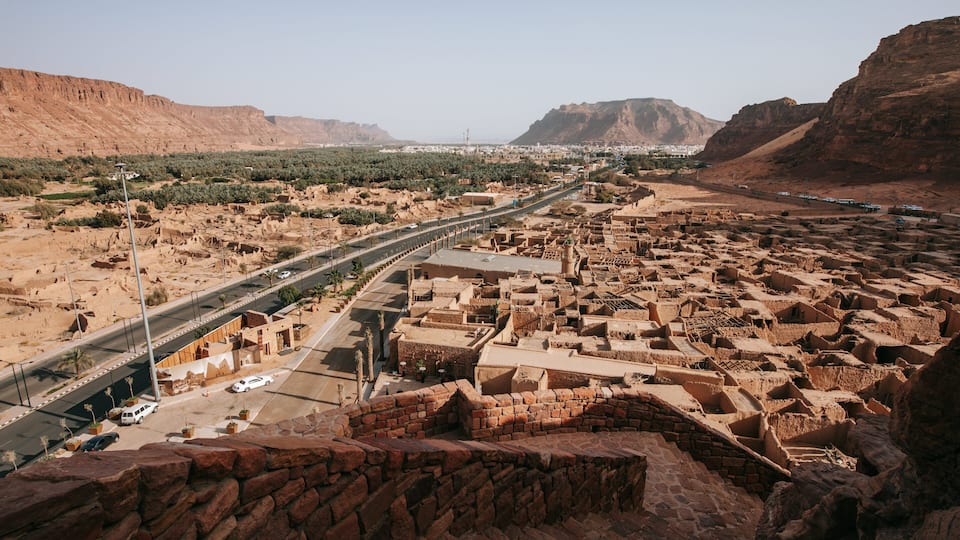 A desert landscape with a modern highway, traditional mud-brick buildings, and distant mountains.