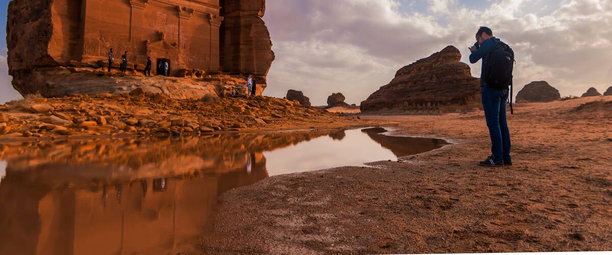 A desert landscape with a large rock formation and a reflective water body.