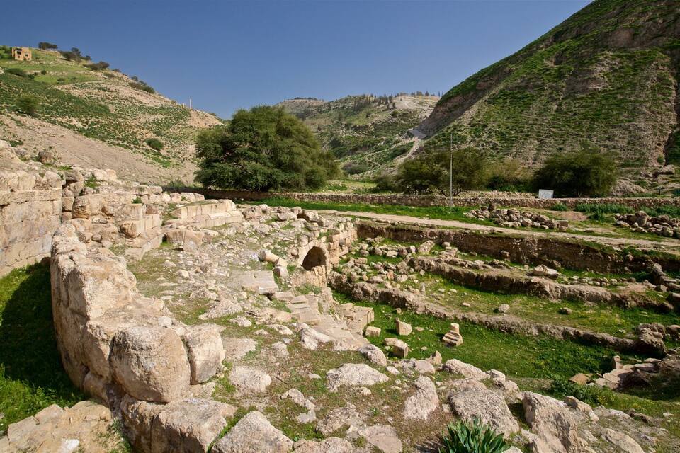 Ruinas antiguas con muros de piedra y una pequeña estructura similar a una cueva en un paisaje montañoso.