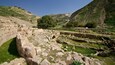Ancient ruins with stone walls and a small cave-like structure amidst a hilly landscape.