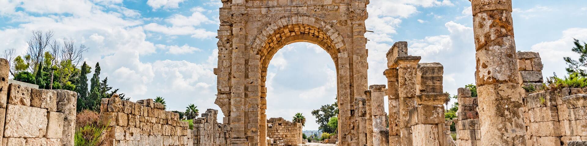 Ancient stone ruins with an arched gateway, surrounded by stone walls and a clear sky.