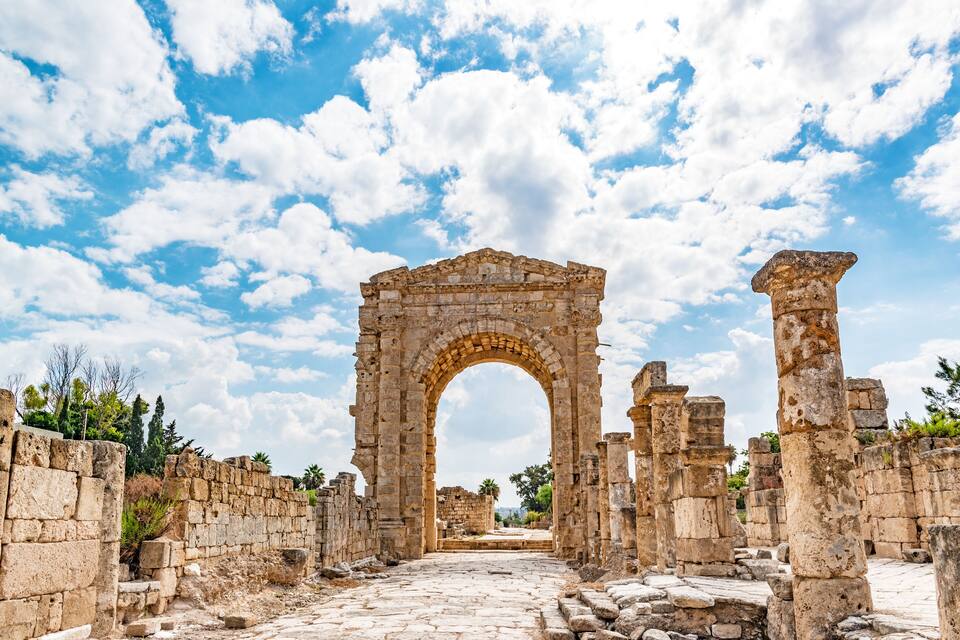 Des ruines anciennes en pierre, avec une porte d’entrée en arc de cercle, entourées de murs de pierre et surplombées par un ciel dégagé.