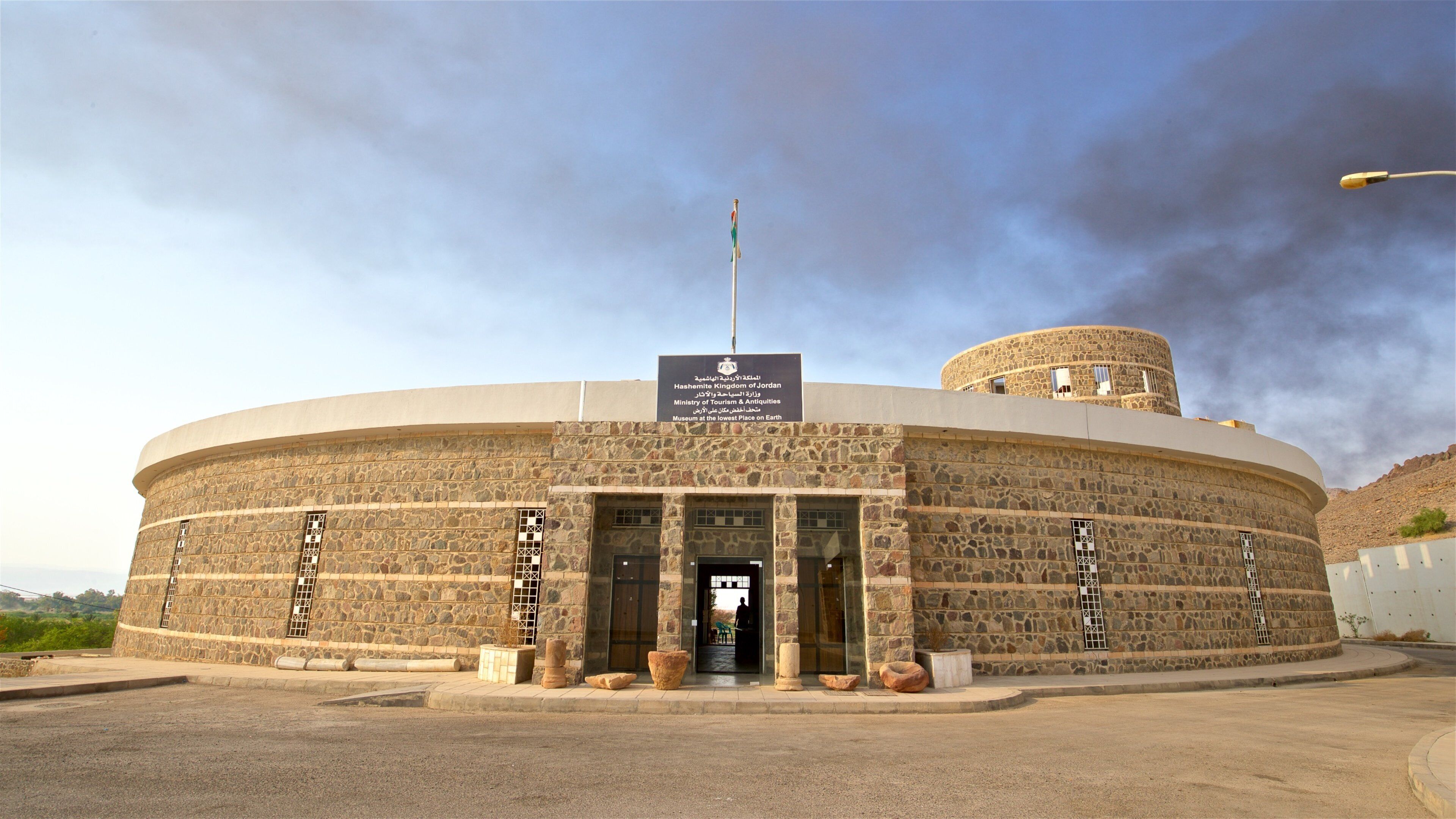 A stone building with a sign reading "Hashemite Kingdom of Jordan Ministry of Tourism & Antiquities Museum at the lowest place on Earth."