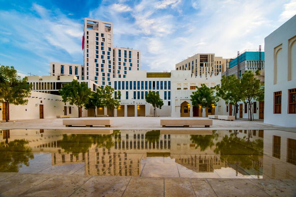 Una plaza urbana moderna con agua reflectante, edificios y árboles.