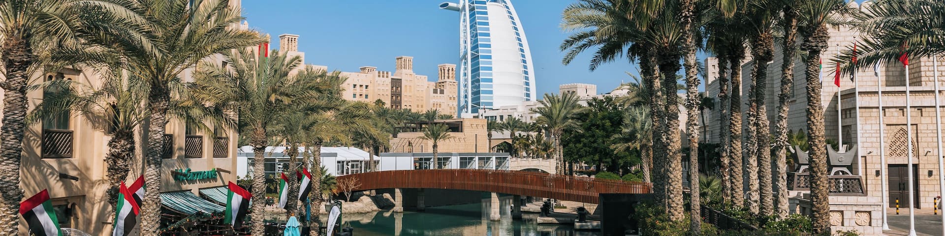 A canal with palm trees, a bridge, and a modern building with a sail-like structure.