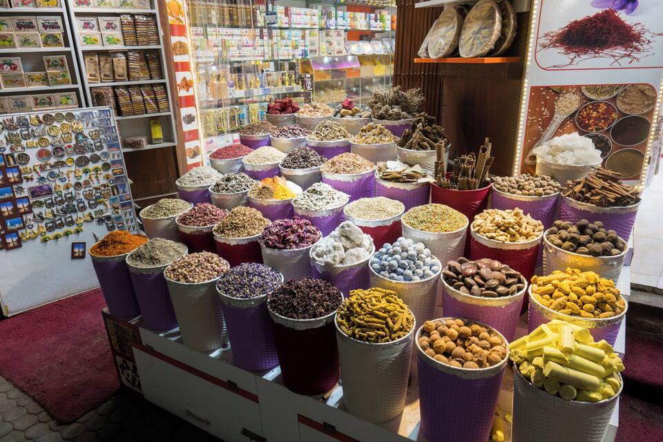 Una tienda de especias con grandes contenedores de diferentes condimentos y una exhibición de especias en la pared.
